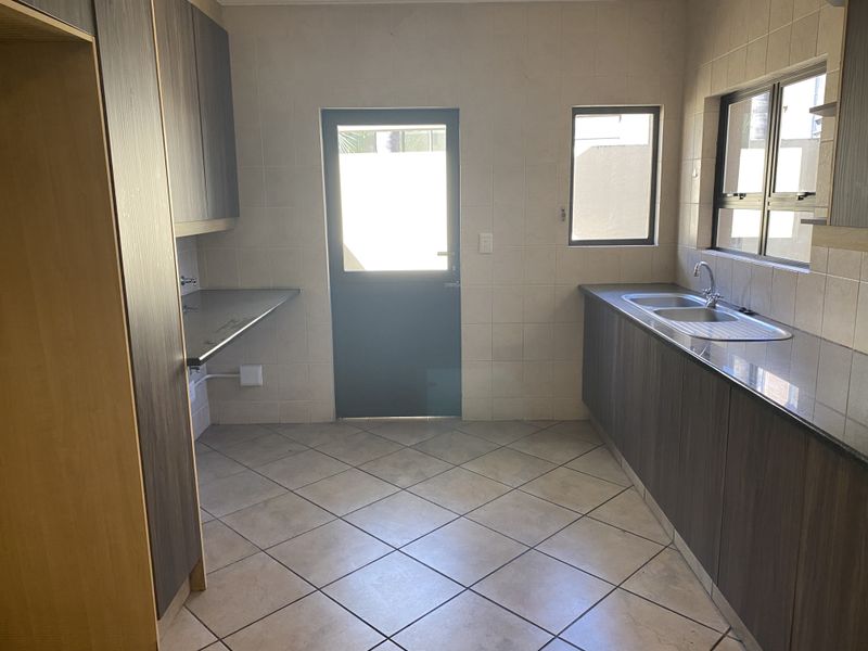 A clean and functional scullery featuring built-in cabinetry, a double sink, tiled splashbacks, and direct access to the exterior.