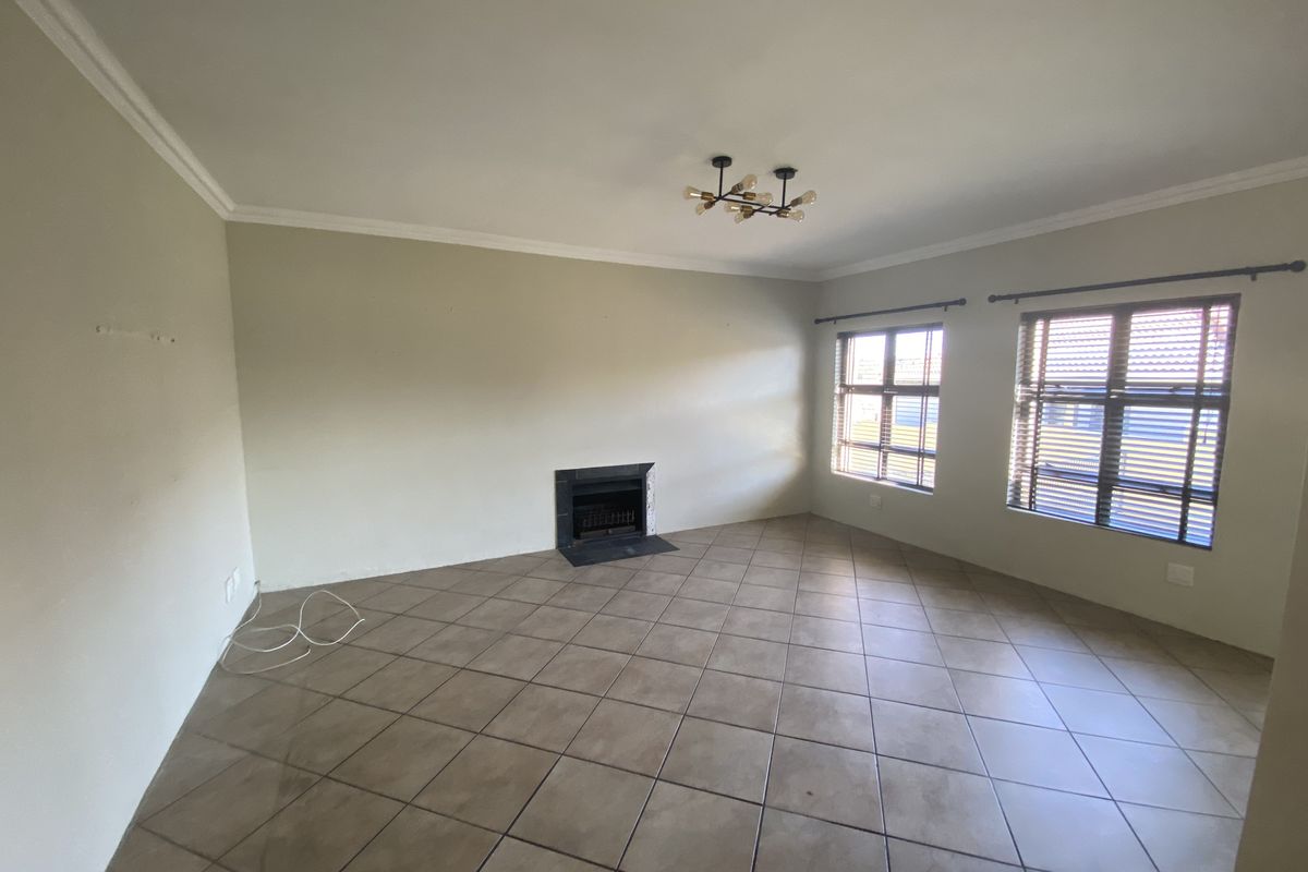 A spacious, empty living room featuring neutral tiled flooring, a built-in fireplace, and large windows with fitted blinds.