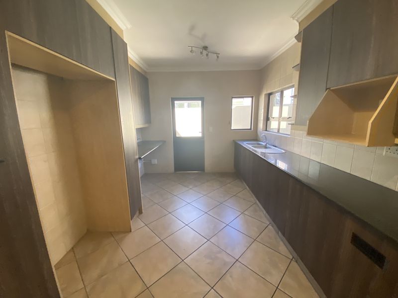A functional scullery area featuring built-in cabinetry, a double sink, tiled flooring, and direct access to the exterior.