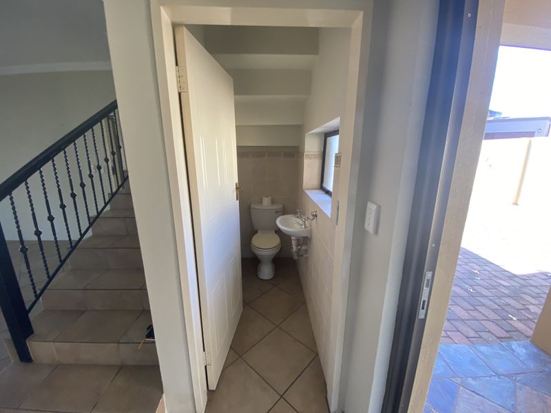 A compact guest bathroom located under the staircase, featuring a toilet and wall-mounted basin with tiled flooring.