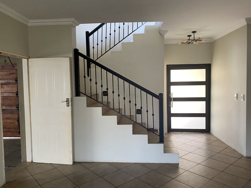 Spacious entrance hall featuring a modern staircase with wrought iron balustrade, tiled flooring, and a contemporary frosted glass front door.