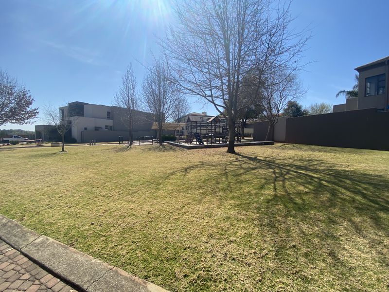 A spacious communal garden area featuring a manicured lawn, perimeter boundary walls, and a dedicated playground structure.