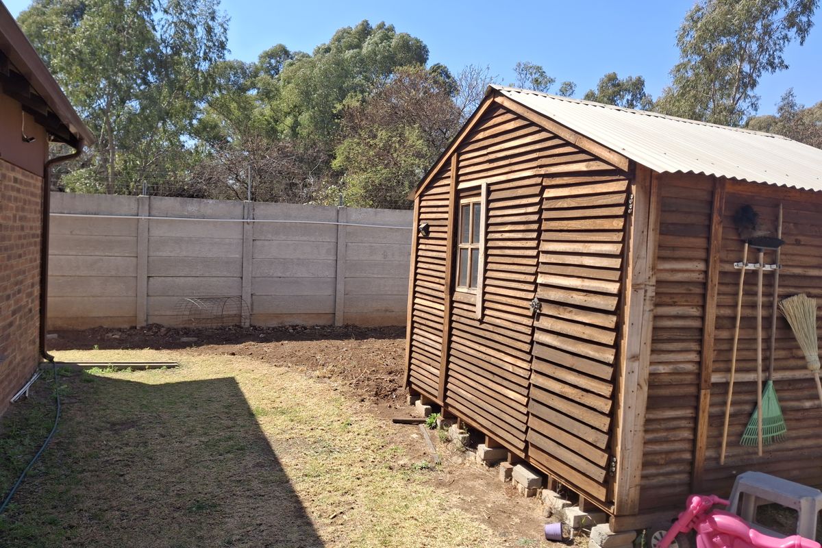 A wooden garden shed situated in the rear yard, featuring timber cladding and a corrugated roof, set against a precast concrete boundary wall.