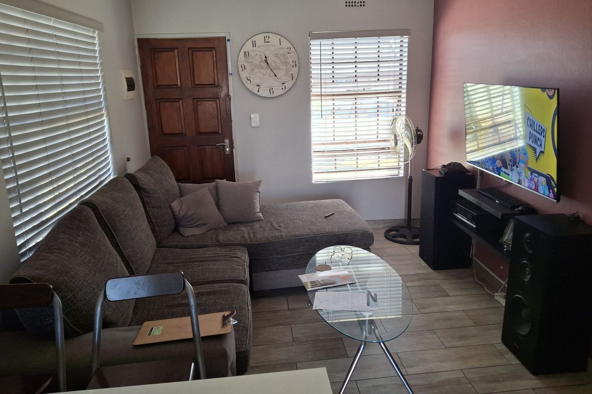 A cozy living room featuring wood-look tile flooring, venetian blinds, and a feature wall, providing a functional and comfortable space.