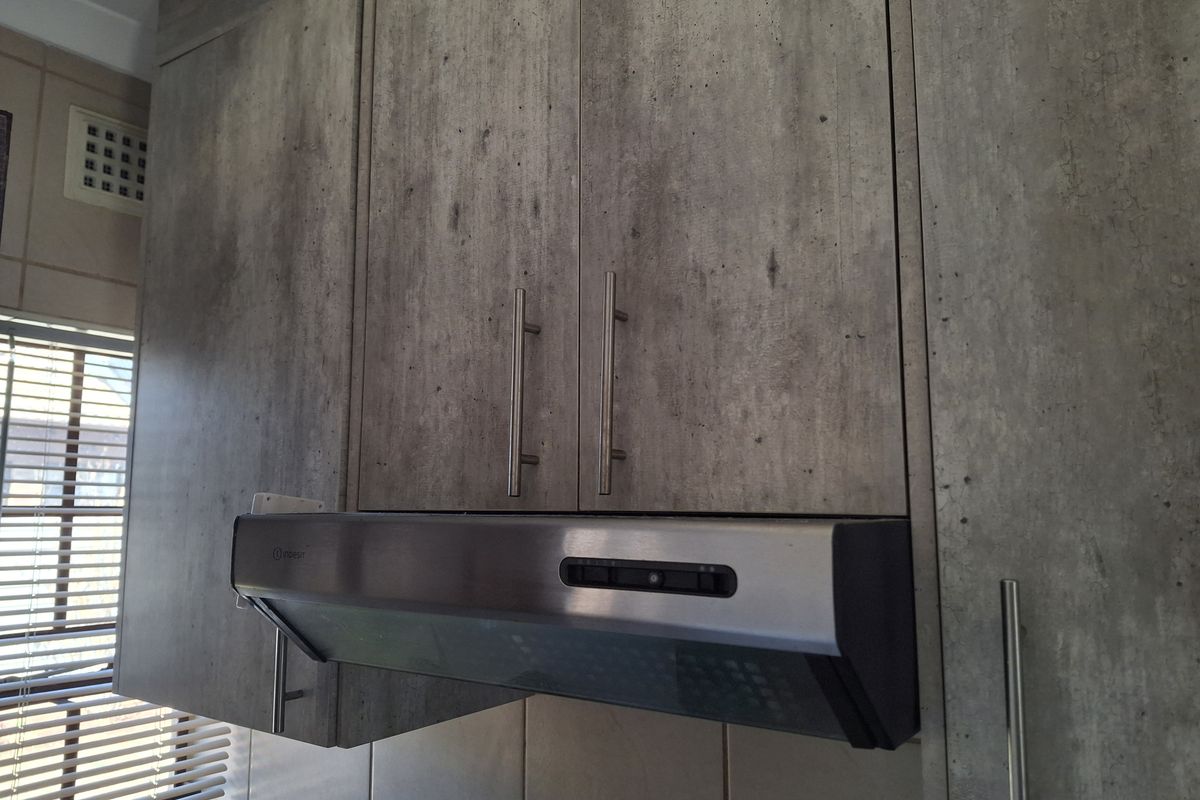 Close-up view of modern concrete-look kitchen cabinetry featuring a stainless steel extractor fan and tiled splashback.