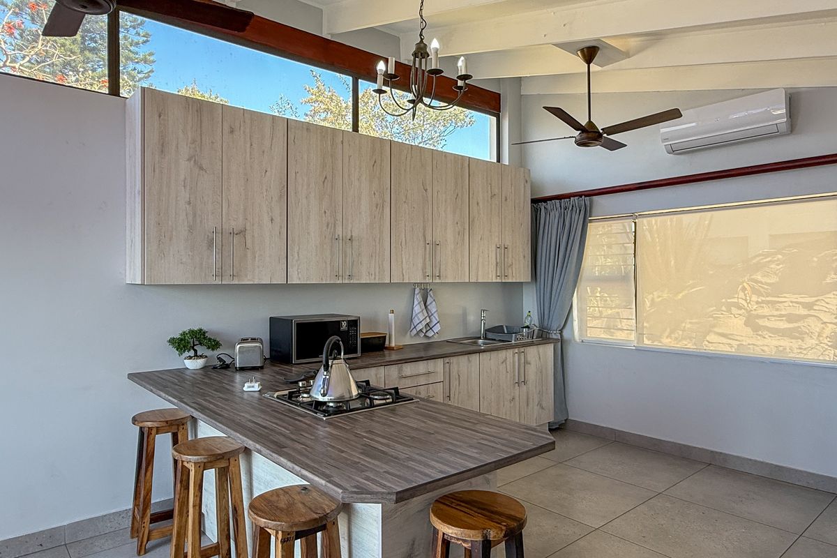 Modern kitchen featuring light wood cabinetry, a breakfast bar with integrated gas hob, tiled flooring, and high clerestory windows providing natural light.