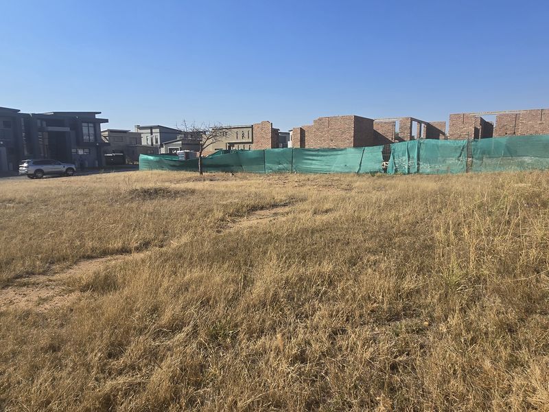 A vacant residential plot featuring a perimeter brick wall with electric fencing, situated in a developed estate with surrounding modern homes.