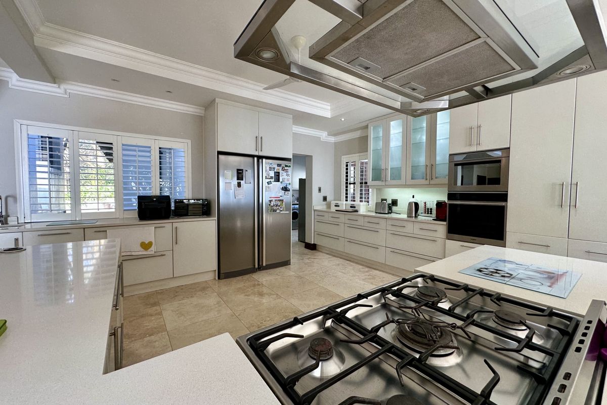 Modern kitchen featuring stone countertops, a central island with a gas hob, stainless steel appliances, and ample cabinetry with integrated lighting.