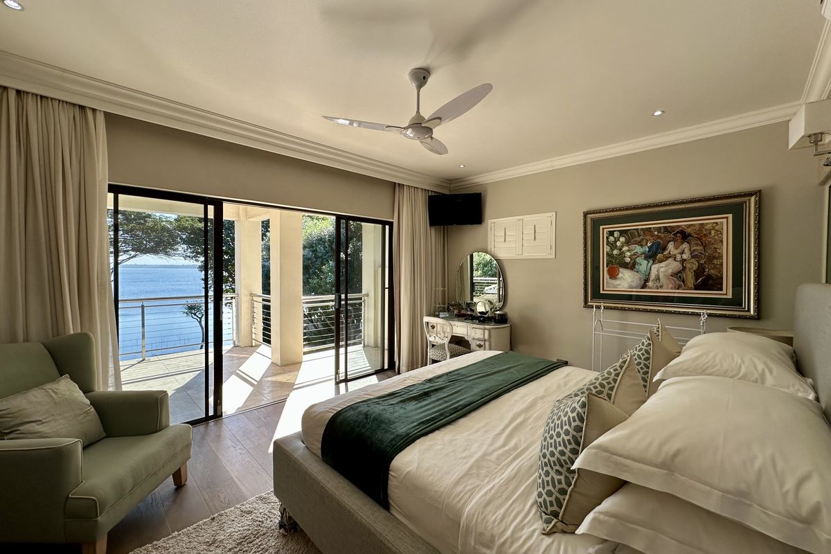 Spacious bedroom featuring sliding glass doors that open onto a private balcony with scenic water views, complemented by recessed lighting and a ceiling fan.