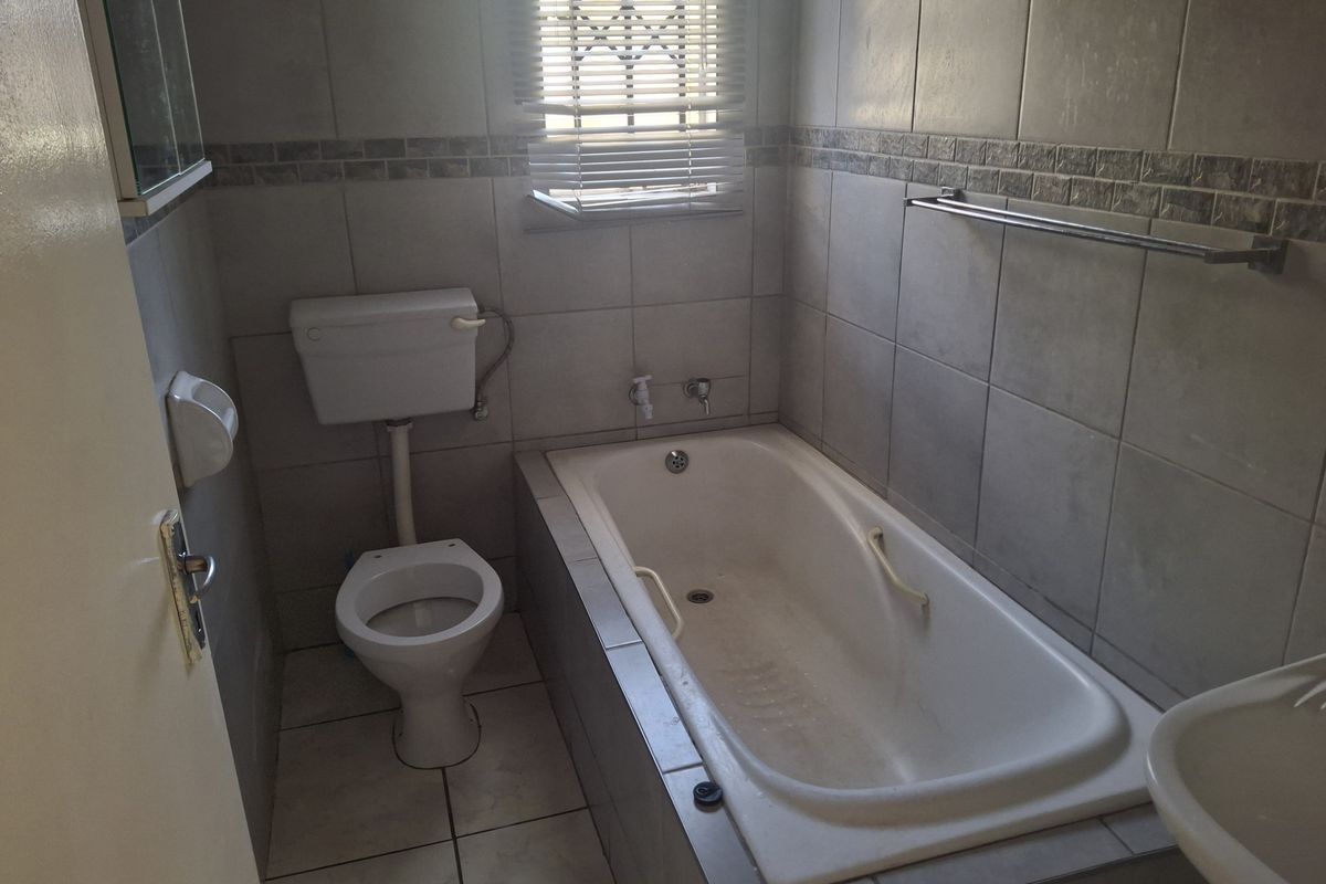 A functional bathroom featuring a built-in bathtub, standard toilet, and tiled walls with a decorative border.