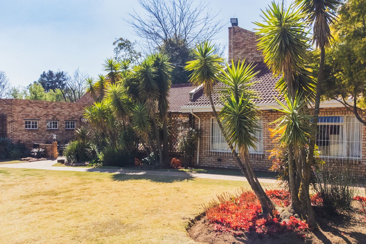 Exterior view of the guest house featuring face-brick facade, tiled roof, and landscaped garden area with mature palm trees and paved walkways.