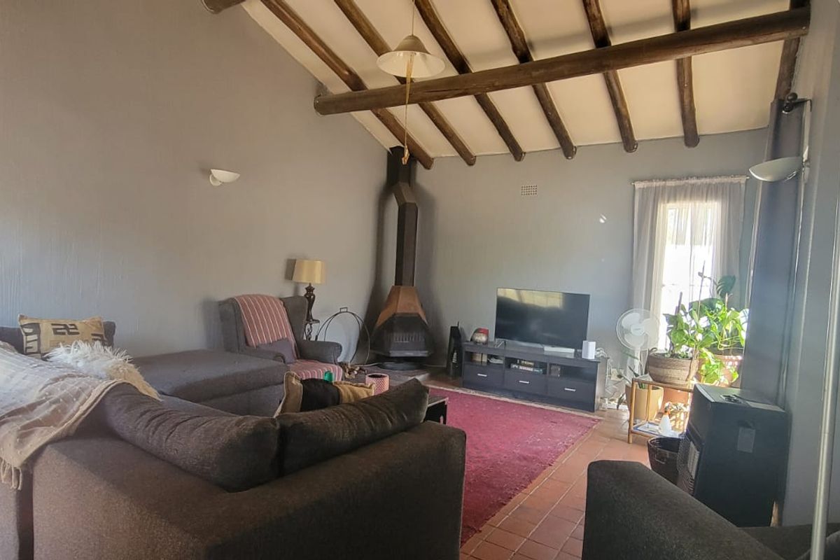 Spacious living room featuring a vaulted ceiling with exposed timber beams, terracotta floor tiles, and a built-in fireplace.