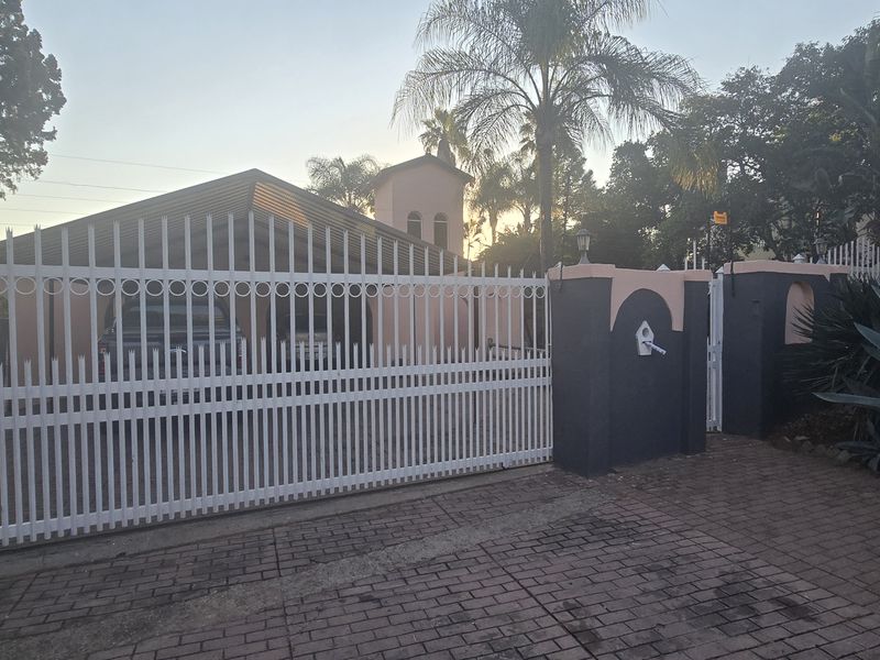 Front view of the property featuring a secure white metal perimeter fence, gated entrance, and paved driveway leading to the main house structure.