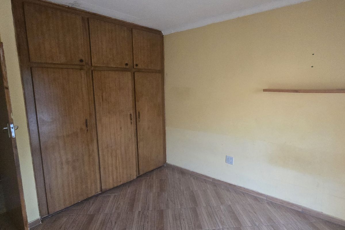 A bedroom featuring built-in wooden cupboards, tiled flooring, and a neutral wall finish, offering a functional space ready for updates.