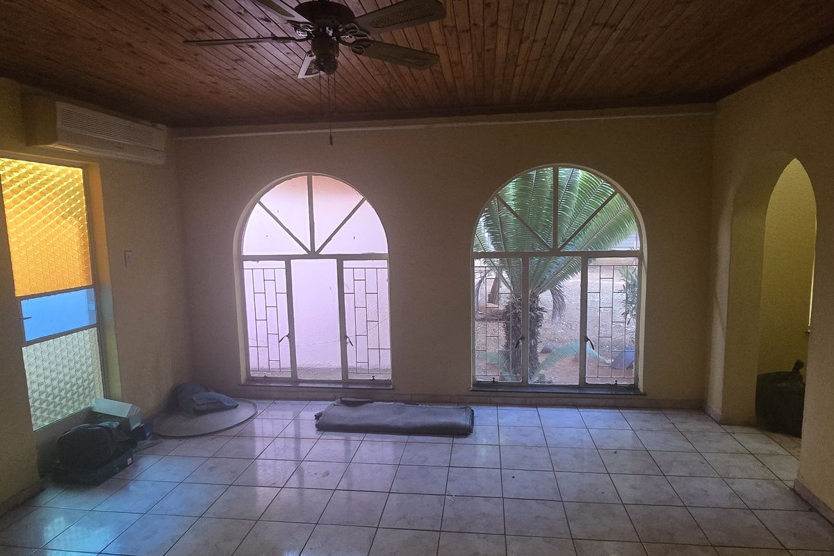 Spacious living area featuring tiled flooring, arched windows with security bars, and a timber-clad ceiling with a mounted ceiling fan.