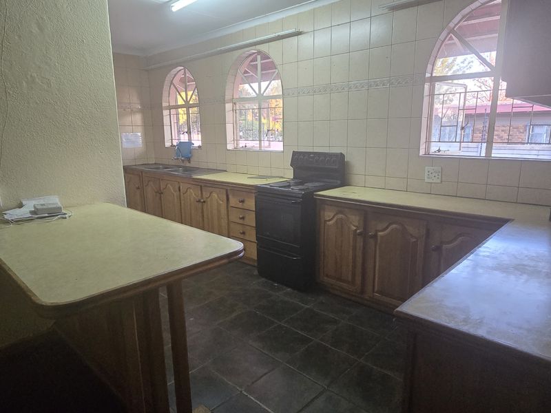 A dated kitchen featuring wooden cabinetry, laminate countertops, tiled walls, and a freestanding stove, offering a functional layout with potential for modernization.