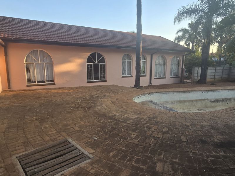 Rear exterior view featuring a paved patio area and an empty swimming pool adjacent to the house with arched windows.