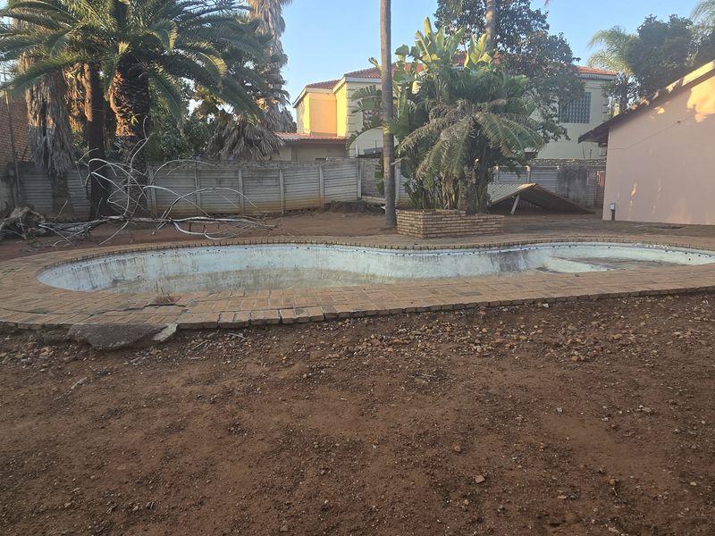 Rear garden area featuring an empty swimming pool with brick coping, set within a large, unlandscaped yard with perimeter walling.