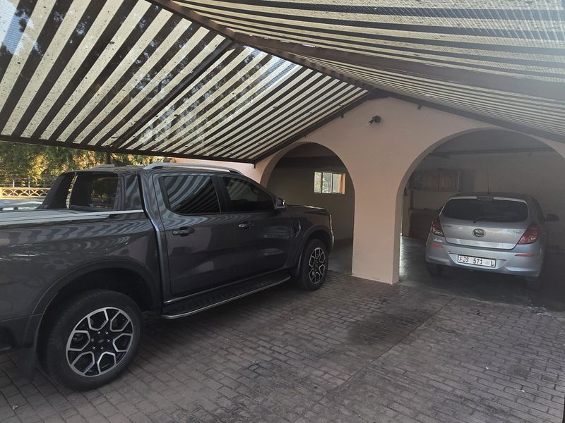 A covered carport area featuring arched structural openings and paved flooring, providing sheltered parking space for multiple vehicles.