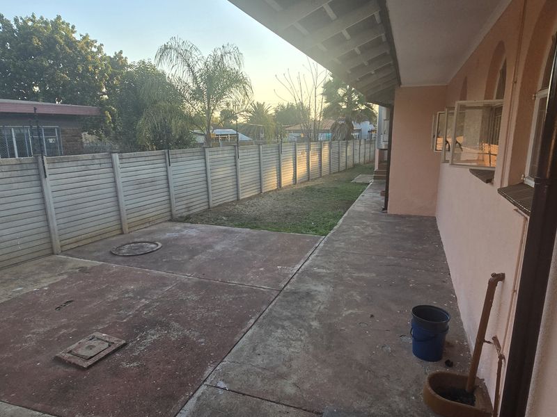 A rear exterior view showing a concrete patio area, perimeter precast walling, and access to the side of the house.