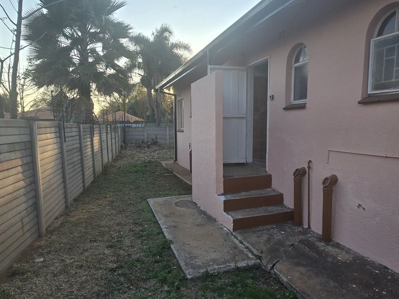 Rear exterior view of the property featuring a concrete pathway, steps leading to an entrance, and a perimeter boundary wall.