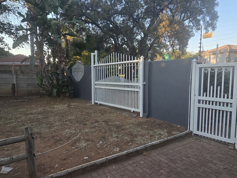 A secure front entrance area featuring a white metal driveway gate and pedestrian gate set within a solid perimeter wall.
