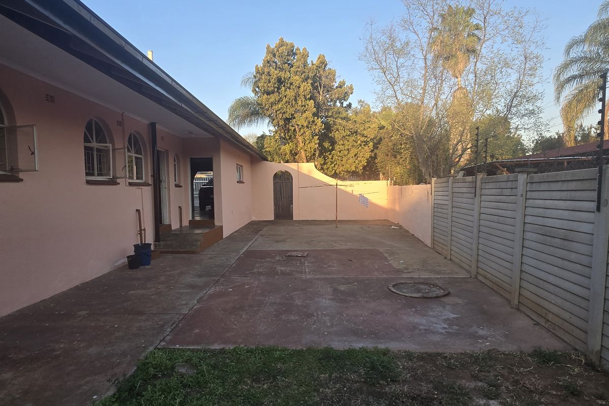 A rear exterior view of the house featuring a paved patio area, perimeter walling, and security fencing.