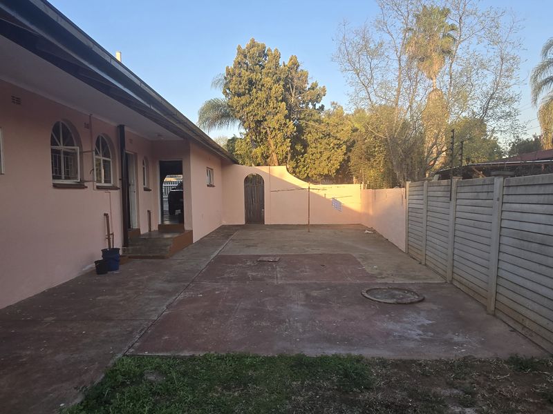 A rear exterior view of the house featuring a paved patio area, perimeter walling, and security fencing.