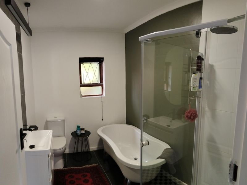 Modern bathroom featuring a freestanding clawfoot bathtub, a separate glass-enclosed shower, a vanity basin, and a toilet with dark tiled flooring.