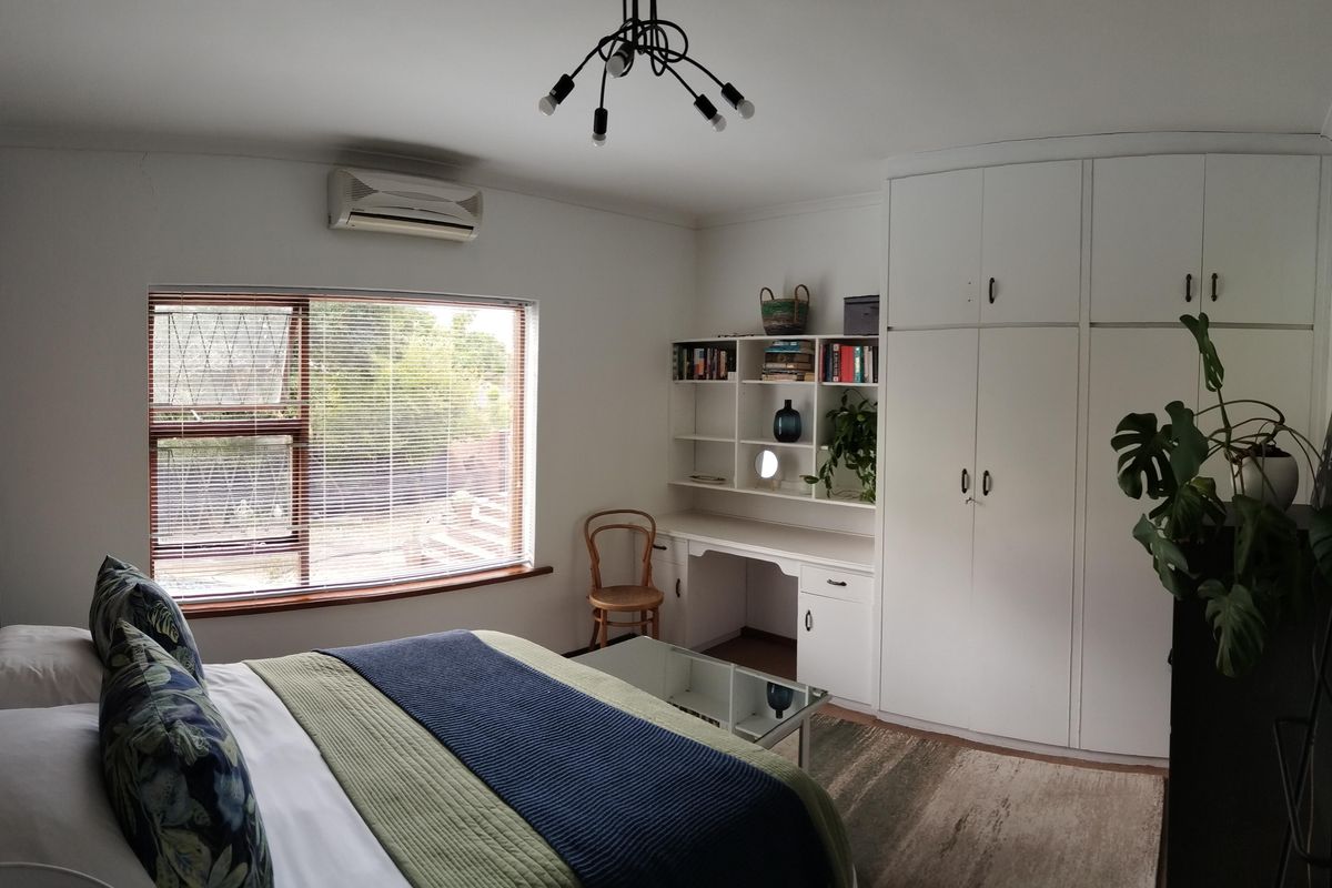 A well-maintained bedroom featuring built-in cupboards, a dedicated study nook with shelving, and a wall-mounted air conditioning unit.