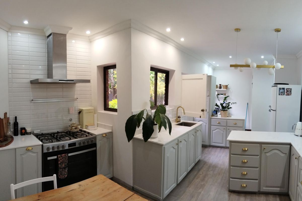 A modern, well-lit kitchen featuring light grey cabinetry, white countertops, a gas stove with stainless steel extractor, and integrated sink area.