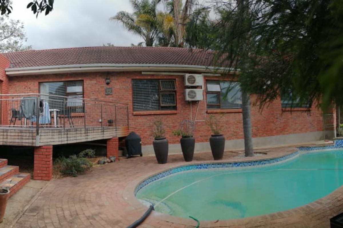 Rear exterior view featuring a red brick house, elevated wooden deck, paved patio area, and a swimming pool.