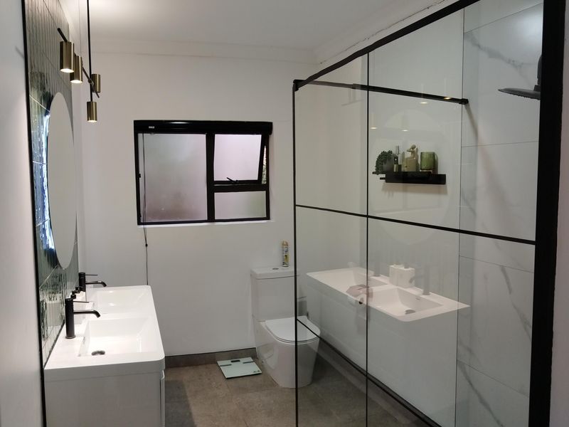 Modern bathroom featuring a double vanity with matte black fixtures, a large walk-in shower with glass enclosure, and contemporary tiling.