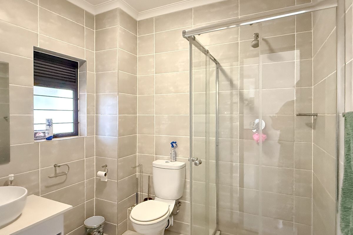 Modern bathroom featuring floor-to-ceiling neutral tiling, a glass-enclosed shower, a contemporary vanity basin, and a toilet.
