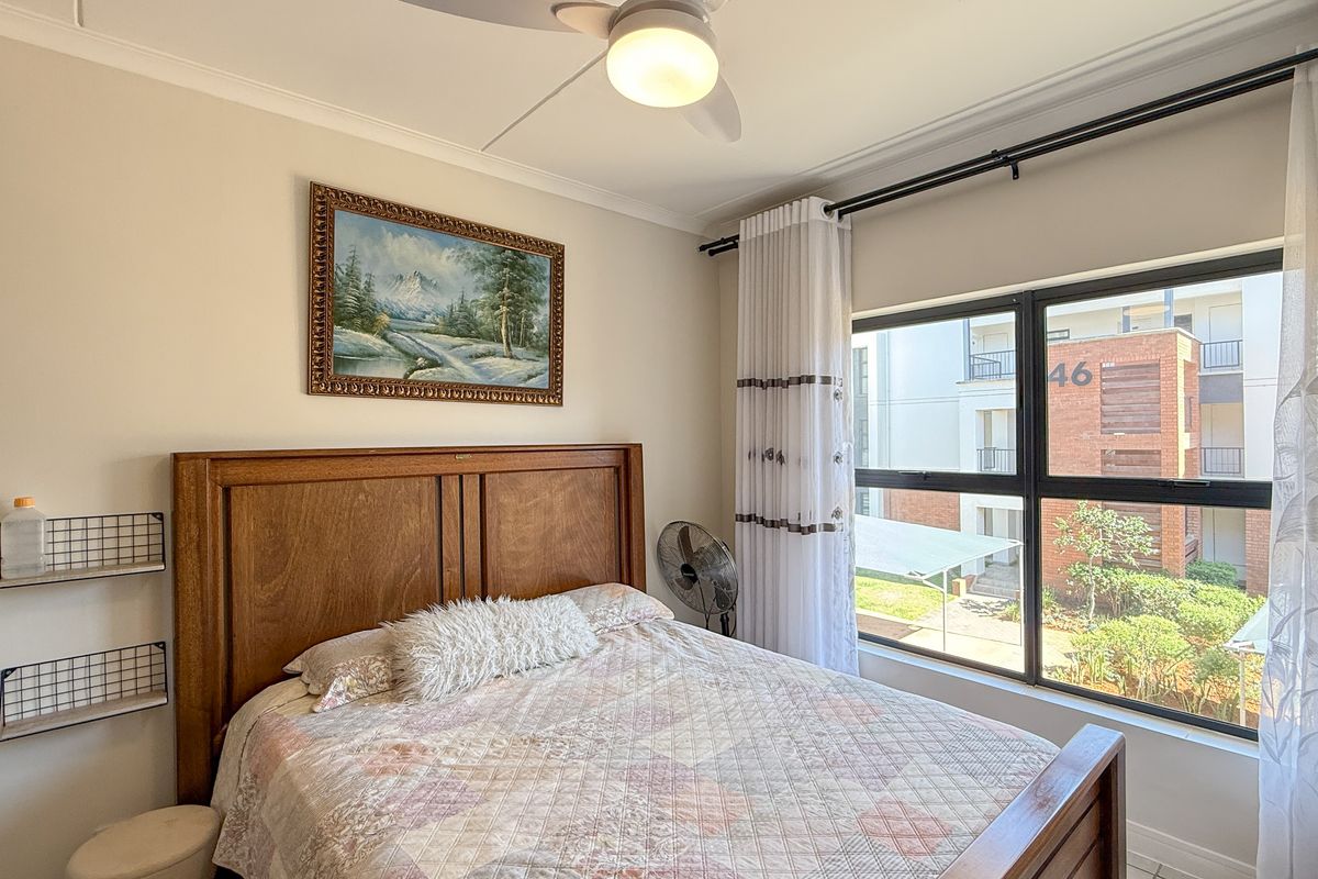 A well-lit bedroom featuring a ceiling fan, large window with curtain tracks, and neutral wall finishes, offering a comfortable living space.
