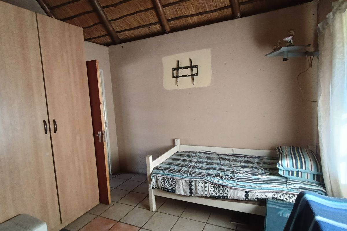 A rustic bedroom featuring a traditional thatched roof, tiled flooring, and a built-in wardrobe, offering a simple and authentic farm-style living space.