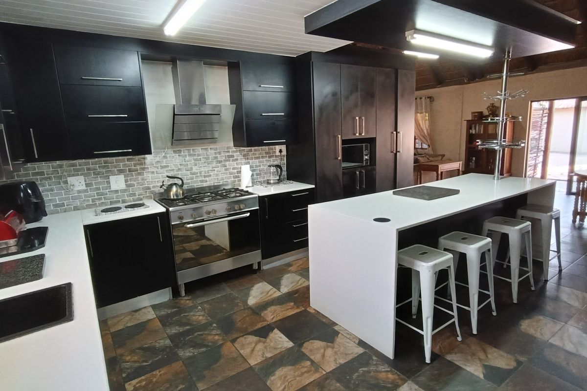 Modern kitchen featuring dark cabinetry, a central island with stone countertop, stainless steel gas stove, extractor fan, and tiled flooring.