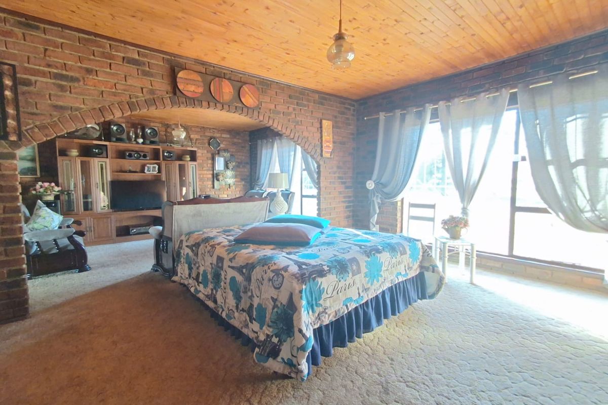 Spacious bedroom featuring exposed brick walls, a vaulted timber ceiling, and large windows allowing for natural light.