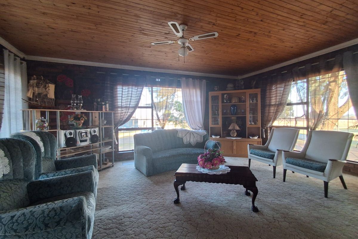 A spacious living room featuring a timber-clad ceiling, ceiling fan, and large windows that provide ample natural light.