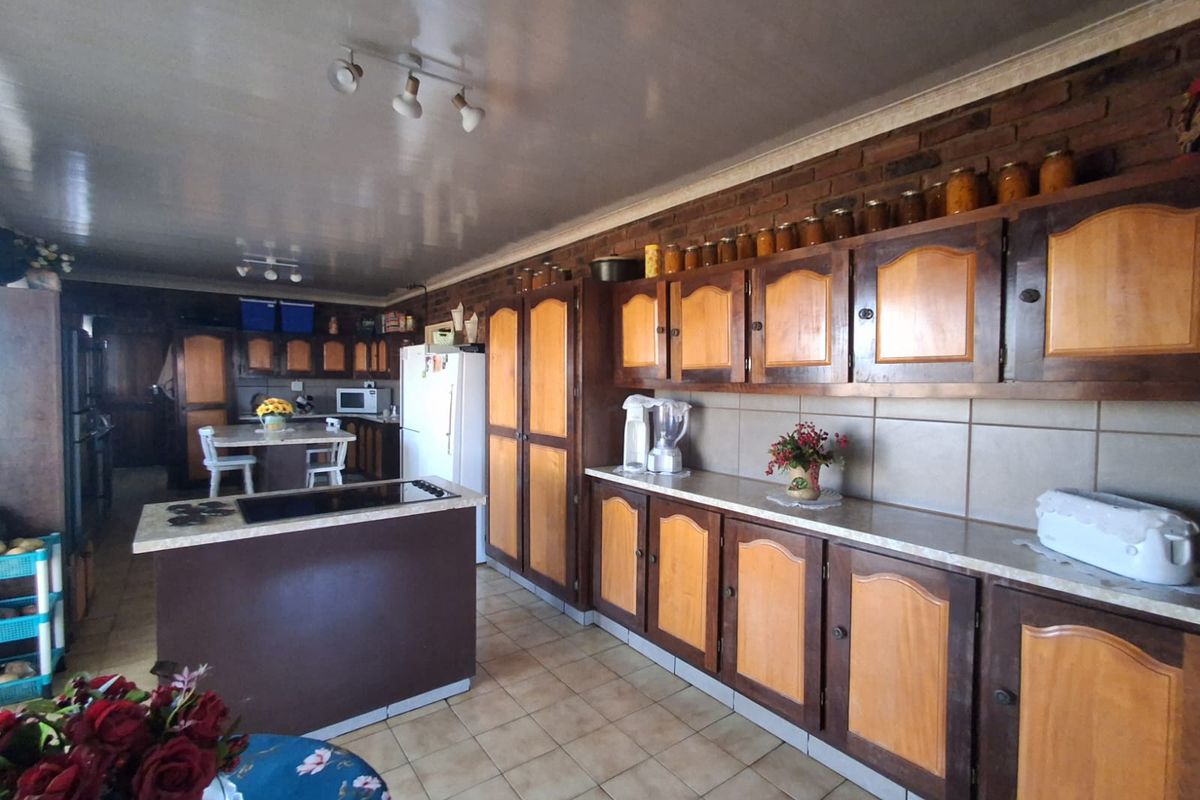 Spacious farmhouse kitchen featuring extensive wooden cabinetry, a central island with integrated cooktop, and a rustic exposed brick wall finish.