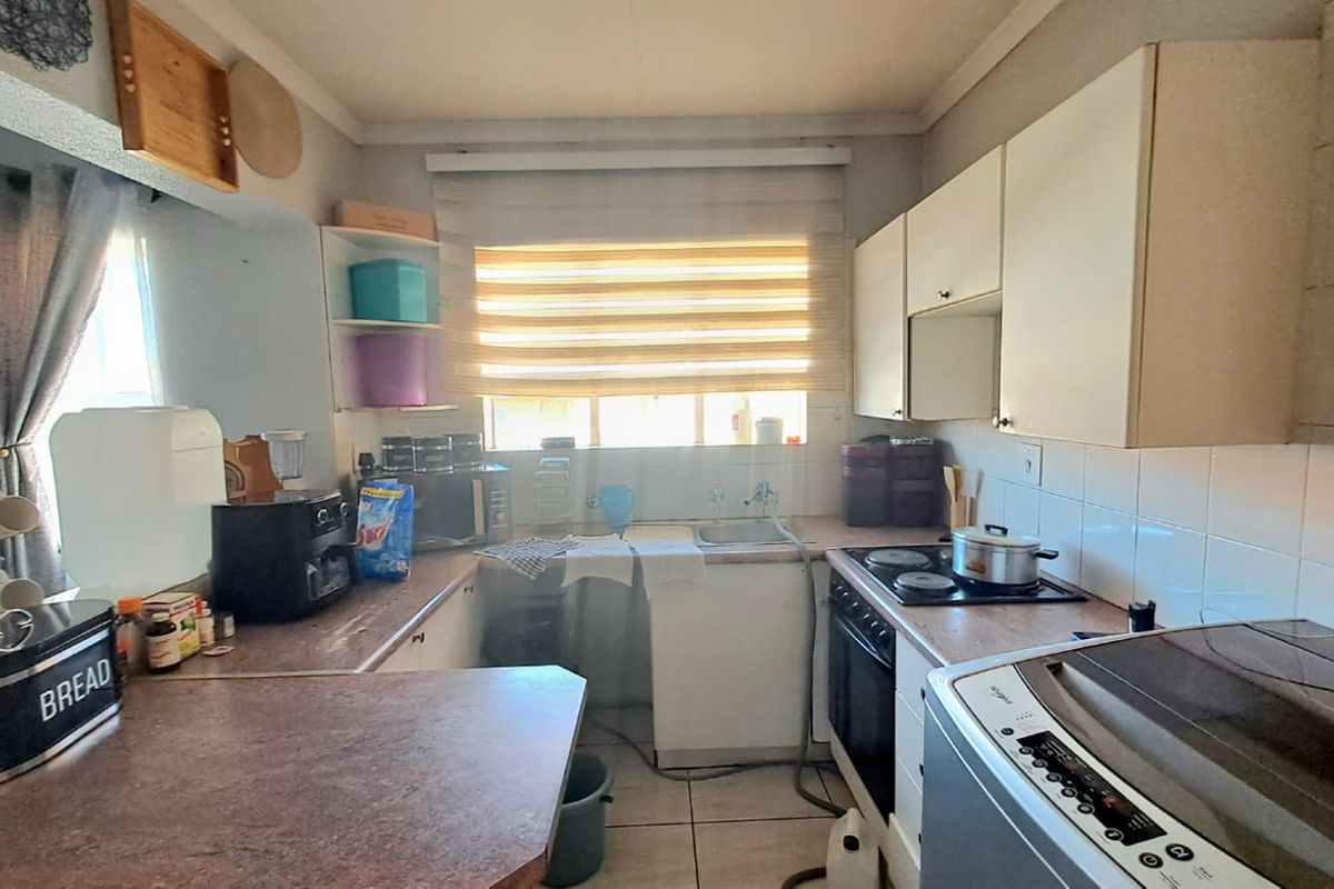A functional kitchen featuring built-in cabinetry, a fitted electric hob and oven, tiled flooring, and a window providing natural light.
