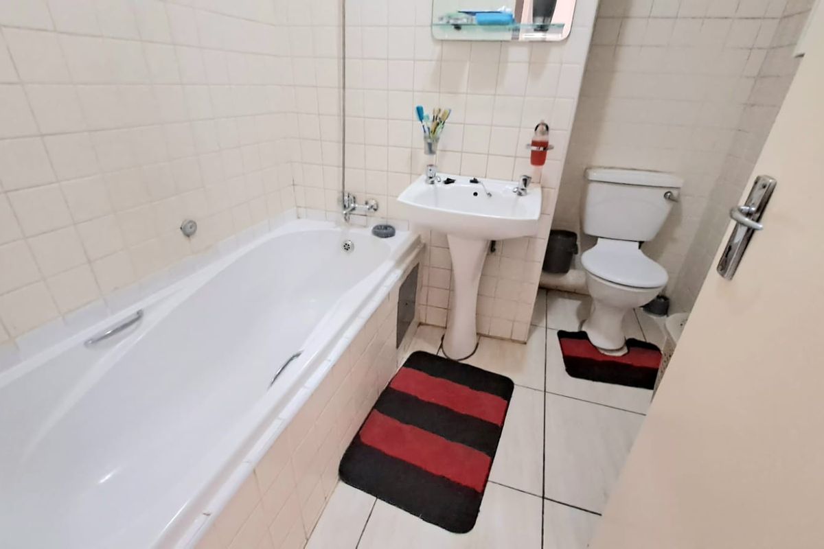 A functional bathroom featuring a standard bathtub, pedestal sink, and toilet with tiled walls and flooring, offering a dated aesthetic ready for modernization.