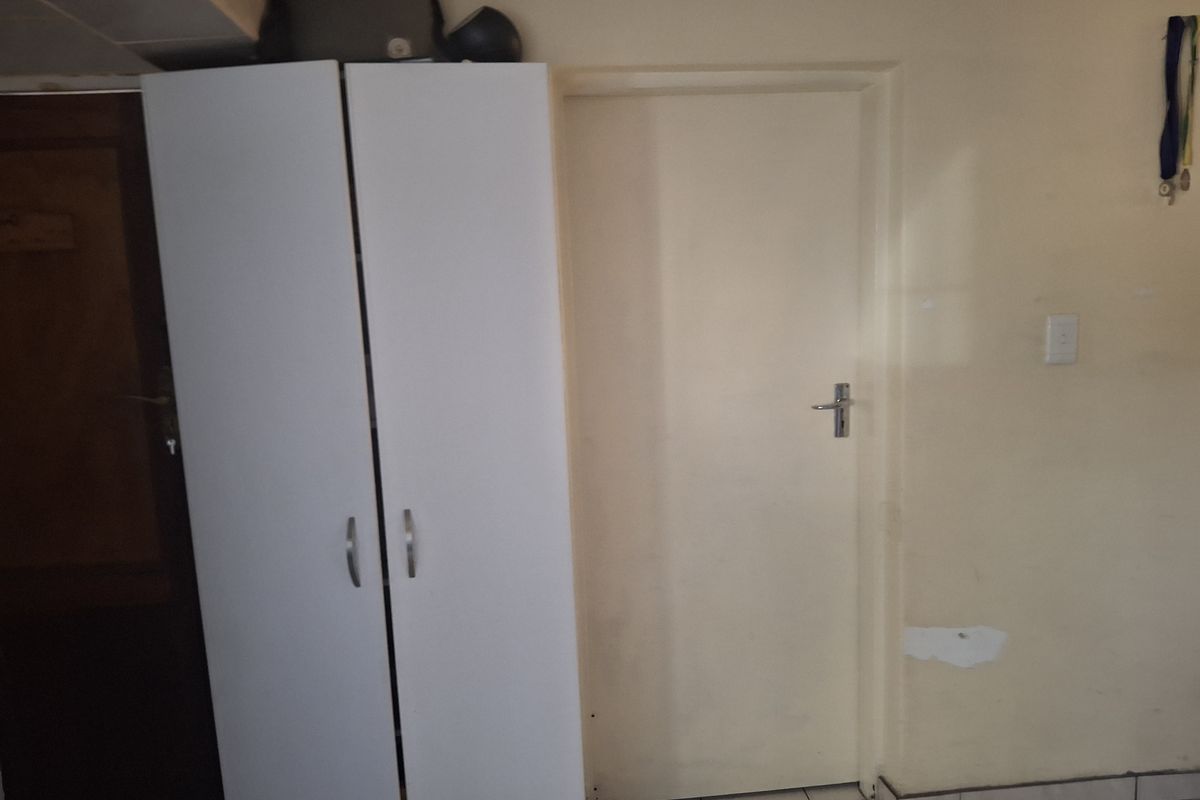 A bedroom interior featuring a built-in white wardrobe and a standard internal door, showing signs of wear on the wall finishes.