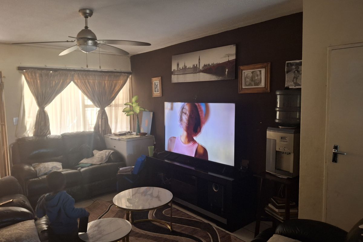 A comfortable living room featuring a ceiling fan, tiled flooring, and a dark accent wall, providing a functional space for relaxation.