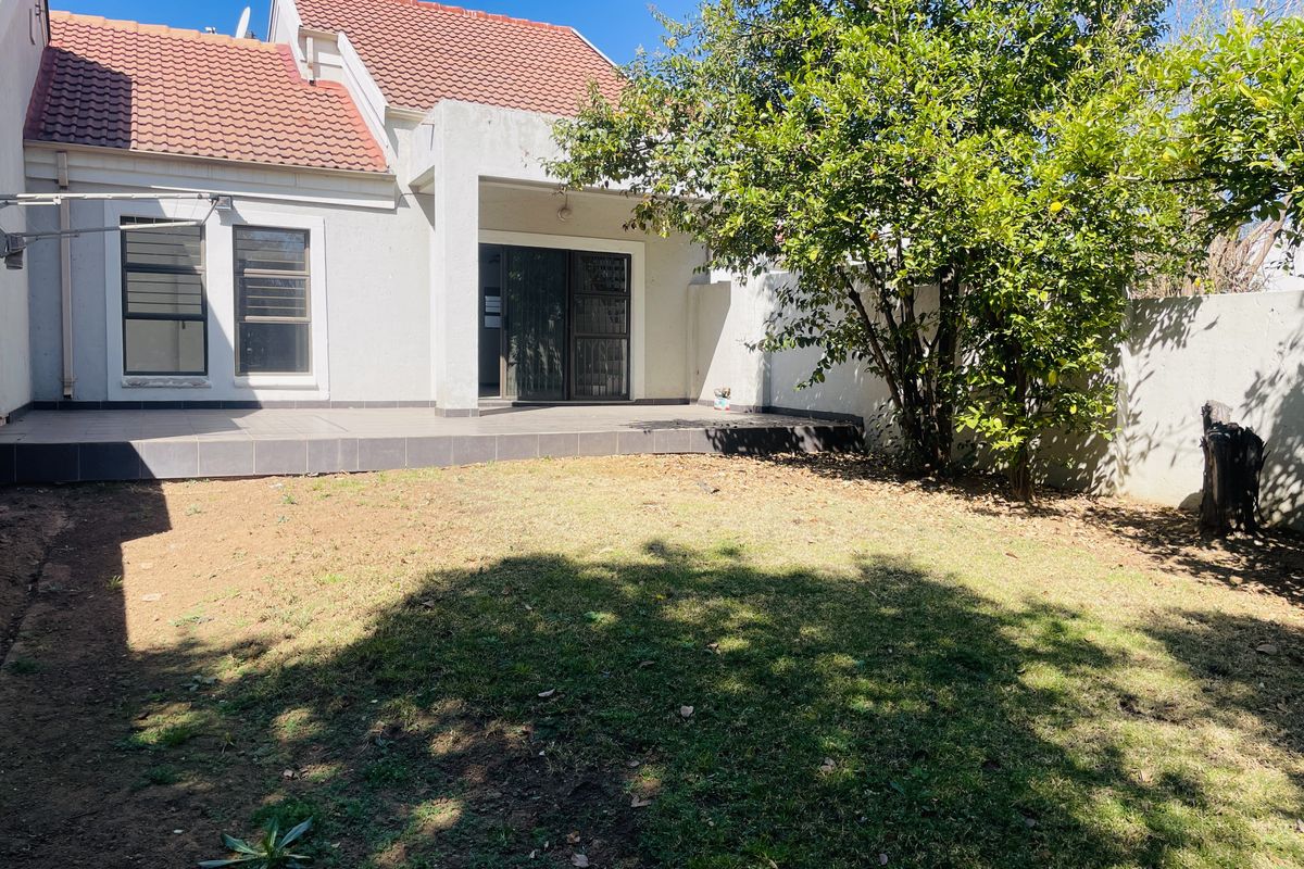 Rear view of the townhouse featuring a paved patio area, a private garden with established trees, and sliding door access to the interior.
