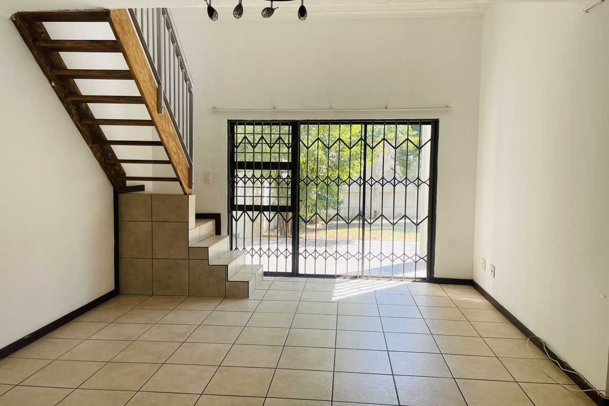 An open-plan living area featuring tiled flooring, a staircase with metal railings, and sliding glass doors with security gates leading to the exterior.