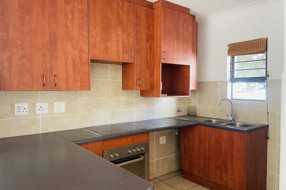 Functional kitchen featuring cherry-wood cabinetry, dark laminate countertops, built-in oven and hob, and tiled splashbacks with a double sink.