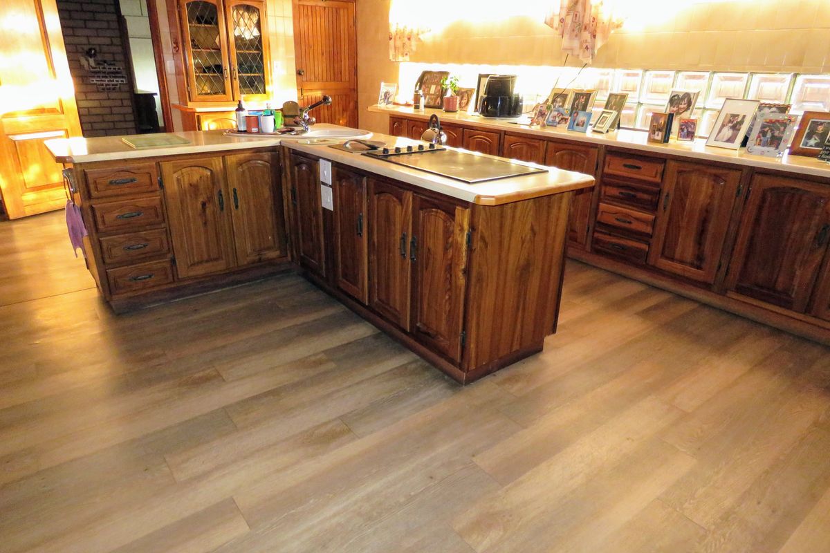 A spacious kitchen featuring traditional timber cabinetry, a central island with a built-in cooktop, and modern wood-look flooring.