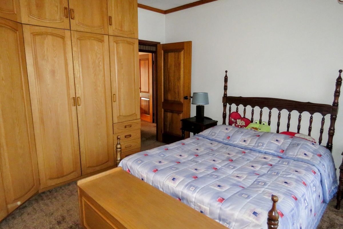 A bedroom featuring built-in wooden cabinetry, carpeted flooring, and traditional wooden door frames.