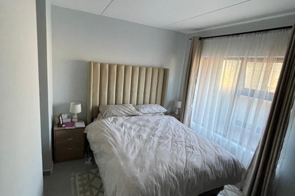 A well-lit bedroom featuring tiled flooring, neutral wall finishes, and a large window with curtain tracks, providing a comfortable and functional living space.